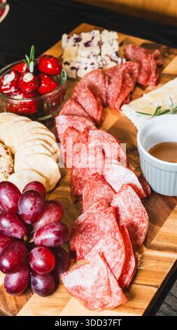 Belle planche de charcuterie avec salami, raisins, craquelins, assortiment de fromages, camembert cuit au four avec sauce aux fruits, fromage à la crème, poivrons farcis et miel Banque D'Images