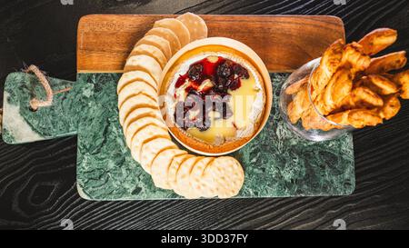 Belle planche de charcuterie avec salami, raisins, craquelins, assortiment de fromages, camembert cuit au four avec sauce aux fruits, fromage à la crème, poivrons farcis et miel Banque D'Images