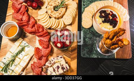 Belle planche de charcuterie avec salami, raisins, craquelins, assortiment de fromages, camembert cuit au four avec sauce aux fruits, fromage à la crème, poivrons farcis et miel Banque D'Images