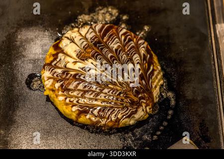L'okonomiyaki est cuit sur une plaque chauffante à Osaka. Préfecture d'Osaka, Japon Banque D'Images