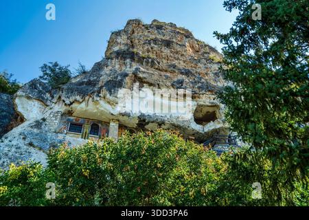 Monastère orthodoxe creusé dans une falaise de calcaire près de Ruse, Bulgarie, entouré de verdure et de ciel bleu, orné de fresques religieuses. Banque D'Images