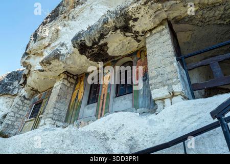 Extérieur du monastère de Basarbovo avec fresques colorées de saint peintes autour de fenêtres cintrées sculptées dans un mur de falaise de calcaire. Banque D'Images