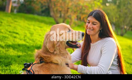 Femme souriant et caressant un chien Golden retriever dans le parc Banque D'Images
