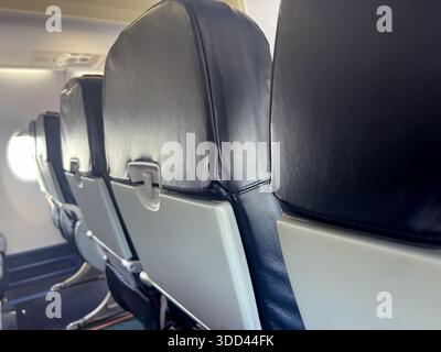 Sièges d'avion vides avec plateaux pliés et éclairage de fenêtre entrant dans la cabine Banque D'Images