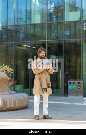 Jeune homme indien touriste discutant sur Internet sur téléphone portable debout à l'extérieur. Joyeux gars hispanique souriant en utilisant le téléphone portable en tapant l'envoi de messagerie électronique Banque D'Images