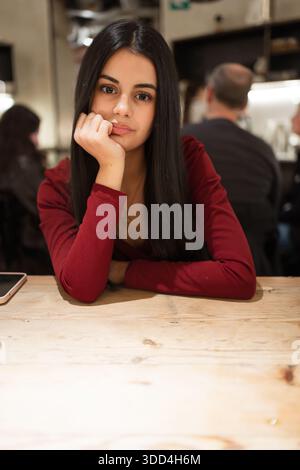 Jeune femme penchée sur la main à une table, regardant pensive dans un restaurant Banque D'Images