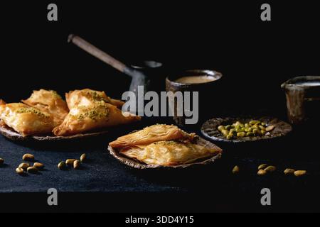 Baklava traditionnel turc fait maison avec pistache servi sur une assiette en céramique avec bol de noix, tasse de café, cezva vintage sur une table en bois noir. Copier l'espace Banque D'Images