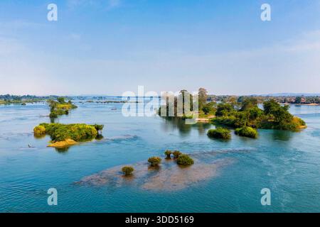 Un large tronçon du fleuve Mékong coule devant des îlots verts éparpillés et une rive bordée d'arbres dans la région des 4000 îles du sud du Laos. La lumière du jour claire et l'eau calme créent un paysage riverain spacieux avec un feuillage éclatant et des reflets doux. Banque D'Images