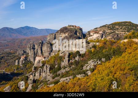 Les monastères historiques de Varlaam et Roussanou se dressent au sommet de spectaculaires pinacles de grès dans les Météores, en Grèce, entourés d'une forêt d'automne dynamique et de chaînes de montagnes lointaines sous un ciel clair. Banque D'Images