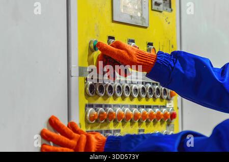 Main dans l'équipement de protection et gants orange pour travailler avec le panneau de commande sur le site de production. Participation des femmes à la production et à l'industrie modernes Banque D'Images