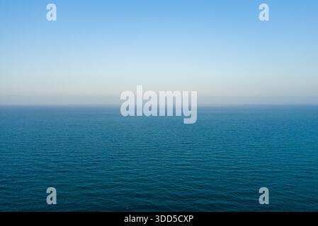 Vue minimaliste sur la mer Méditerranée avec de douces ondulations s'étendant vers un horizon serein sous un ciel bleu clair et dégradé. La scène tranquille évoque un sentiment de calme et de possibilité infinie. Banque D'Images