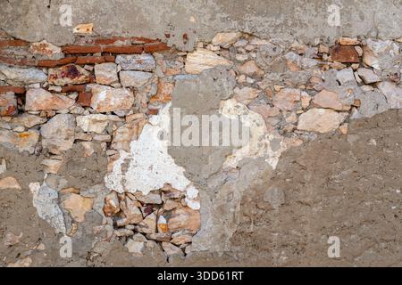 Un mur présente un mélange de pierres et de plâtre avec une texture et des couleurs visibles. Cette scène se produit sur un chantier de construction pendant la journée, montrant des travaux Banque D'Images