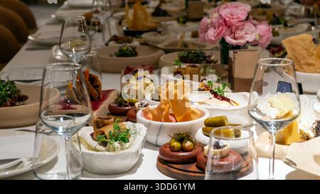 Table de banquet de luxe avec hors-d'œuvre méditerranéens mezze, centres de table roses et vin créant une atmosphère élégante pour les événements dînatoires Banque D'Images
