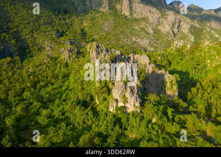Des formations calcaires pointues s'élèvent au-dessus d'une jungle verte dense dans la région de Konglor au centre du Laos. La lumière chaude du soleil souligne le contraste spectaculaire entre roche accidentée et végétation tropicale vibrante dans ce paysage karstique d'Asie du Sud-est. Banque D'Images