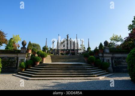 De larges marches en pierre mènent à une terrasse ornée de statues classiques et de verdure luxuriante dans les jardins Borroméens historiques. La lumière du soleil tôt le matin projette des ombres nettes, soulignant la symétrie et le design formel de ce monument italien. Banque D'Images