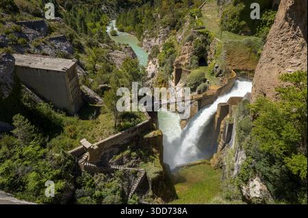 Une puissante cascade se déverse d'un barrage en béton dans une gorge rocheuse escarpée, entourée d'une végétation dense et de falaises spectaculaires à Las Penas. Les textures ensoleillées de pierre, d'eau et de forêt créent un paysage naturel saisissant. Banque D'Images