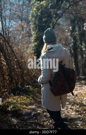 Fille avec chapeau et sac à dos en cuir marche sur une route de montagne. Randonneur féminin en hiver promenades dans la nature. Isolement, solitude, paix et silence. Banque D'Images