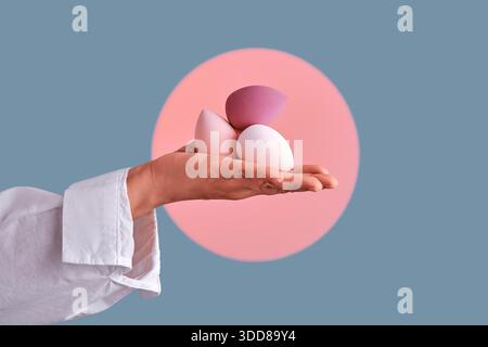 Main tenant trois éponges de maquillage colorées différentes sur un fond pastel, représentant la beauté et l'application cosmétique Banque D'Images