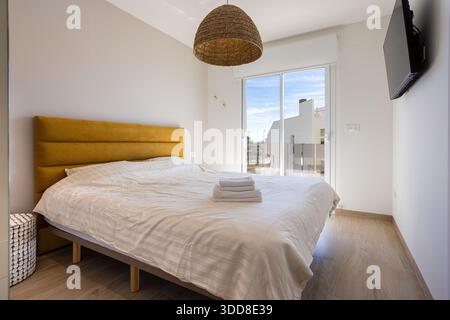 Chambre confortable avec lit moutarde, lumière naturelle, plancher de bois et porte coulissante balcon Banque D'Images
