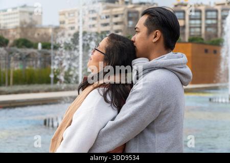 Heureux homme asiatique et femme embrassant sur le parc tout en regardant l'horizon avec espoir Banque D'Images