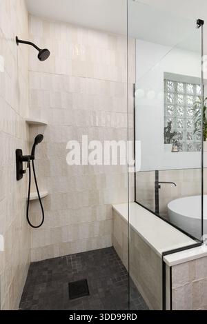 Une élégante douche de salle de bains avec carrelage texturé marron vertical, carrelage carré gris foncé, robinets noirs et murs blancs. Banque D'Images