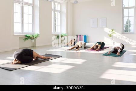 Cours de yoga en groupe à Childs pose dans un studio lumineux et serein rempli de rayons de soleil Banque D'Images
