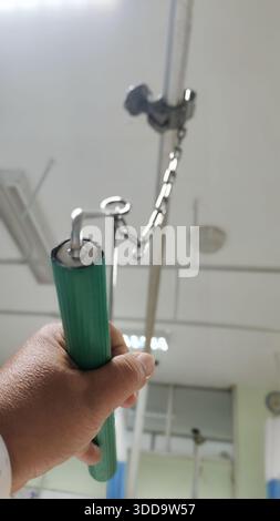 Gros plan en angle bas de la main d'un patient tenant fermement une poignée de traction ou de traction verte fixée à une chaîne métallique dans un coffret d'hôpital Banque D'Images