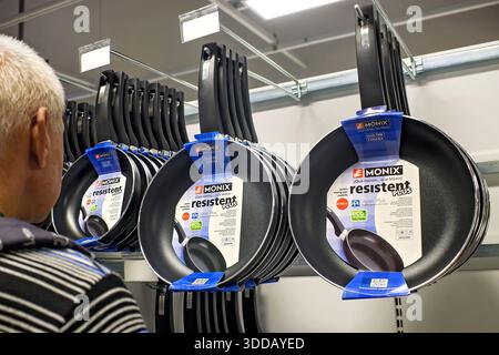 Sliema, Malte - 24 décembre 2025 : un homme examine un présentoir de poêles antiadhésives Monix Resistent plus suspendues dans un rayon de magasin. Banque D'Images