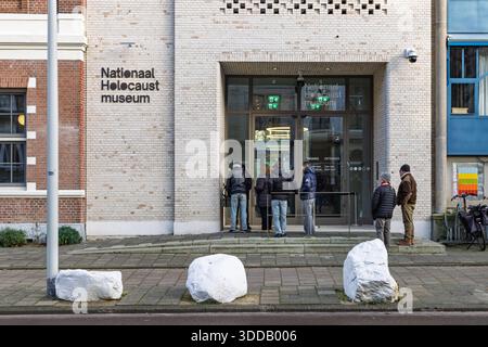 Les gens attendent pour entrer au Musée national de l'Holocauste à Amsterdam, avec une façade en briques blanches et des portes d'entrée en verre. Banque D'Images