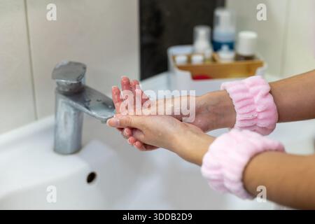 Gros plan des mains de la femme en train d'être lavées. Les mains féminines étant lavées sous l'eau courante dans la salle de bain, favorisant l'hygiène et la propreté, avec du rose Banque D'Images