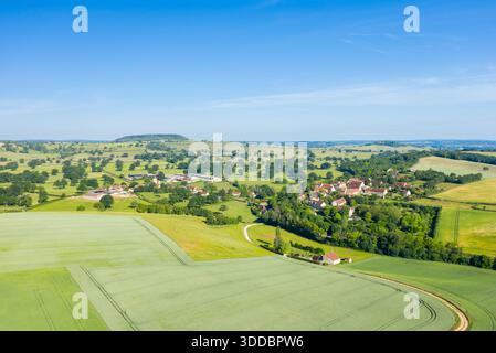 Prise de vue par drone à grand angle du village de Cuncy les Varzy niché au milieu de terres agricoles verdoyantes, de haies et de collines ondulantes sous un ciel bleu vif. Banque D'Images