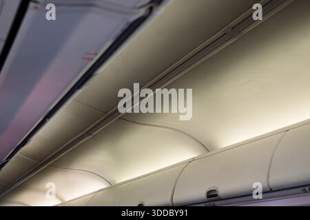 Vue rapprochée de l'intérieur d'une cabine d'avion, avec des rangées de compartiments à bagages suspendus et des panneaux de plafond avec bandes lumineuses lumineuses lumineuses. La COM Banque D'Images