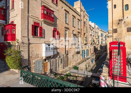 Rue de la Valette avec bâtiments historiques, cabine téléphonique rouge, et balcons colorés, Malte. Banque D'Images
