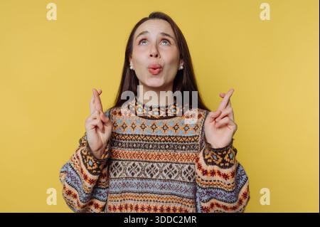 Femme en pull à motifs croisant les doigts sur fond jaune Banque D'Images