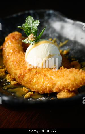 Un dessert avec une banane, une crème glacée et de la crème fouettée sur le dessus. Le dessert est servi dans un bol noir Banque D'Images