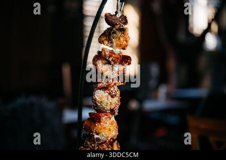 Une brochette de nourriture est suspendue à une tige métallique. La nourriture est un mélange de viande et de légumes, et il est grillé. La scène se déroule dans un restaurant, avec un di Banque D'Images