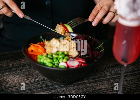Une personne mange un bol de nourriture avec une fourchette. Le bol contient une variété de légumes, y compris des carottes, des radis et des brocolis. La personne est usi Banque D'Images