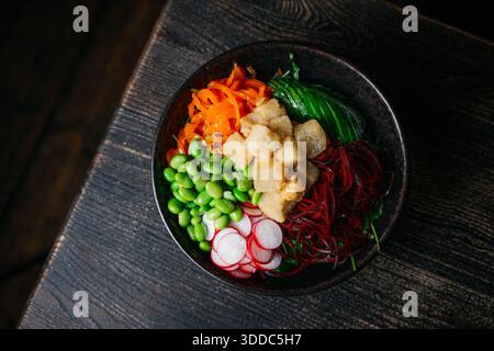 Un bol de nourriture avec une variété de légumes, y compris des carottes, des radis et des algues. Le bol est sur une table en bois Banque D'Images