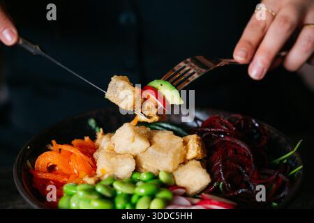 Une personne mange une salade avec une fourchette. La salade est pleine de légumes, y compris des carottes, du brocoli et du chou rouge. La personne tient une fourchette Banque D'Images
