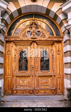 31 octobre 2025, Tbilissi, Géorgie : double porte en bois ornée avec des sculptures complexes, des grilles en fer forgé et une fenêtre de tableau arrière cintré Banque D'Images