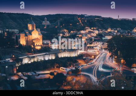 La vieille ville de Tbilissi brille la nuit avec des traînées légères de voitures en mouvement, mettant en valeur l'église Metekhi Banque D'Images