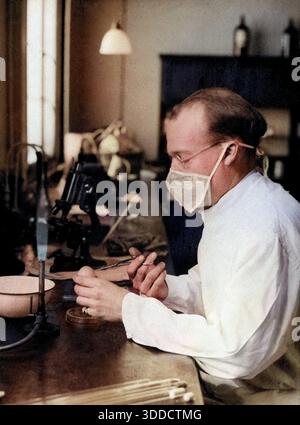 Fièvre jaune : un scientifique portant un masque facial travaille sur un banc de laboratoire avec des brûleurs de bunsen et des microscopes, vers 1910/1930. Banque D'Images