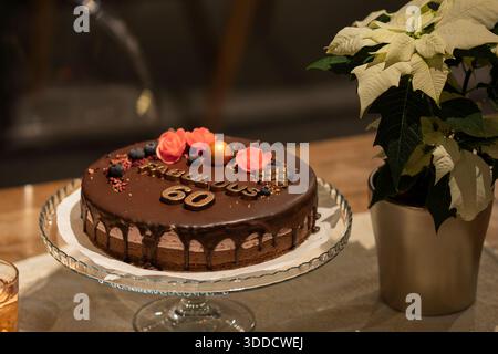 Élégant gâteau d'anniversaire au chocolat décoré de fleurs, de baies et de détails dorés célébrant un 60e anniversaire. Gâteau au chocolat de luxe. Banque D'Images