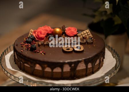 Élégant gâteau d'anniversaire au chocolat décoré de fleurs, de baies et de détails dorés célébrant un 60e anniversaire. Gâteau au chocolat de luxe. Banque D'Images