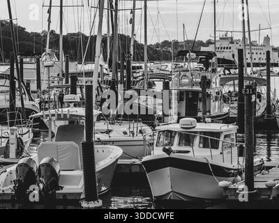 Les bateaux sont amarrés étroitement à une marina de long Island, formant une scène dense et monochrome de mâts, de quais et de navires. Un ferry entre par l'extrême droite Banque D'Images