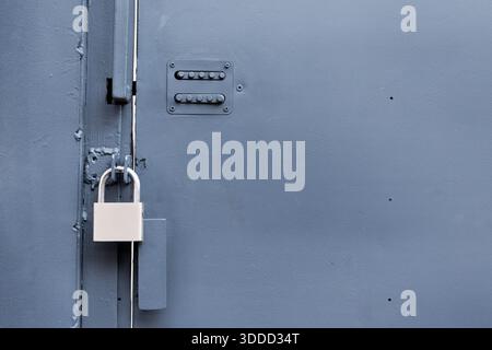 Porte en métal gris offrant sécurité et accès contrôlé, dotée d'un cadenas fermé et d'un ancien clavier mécanique Banque D'Images