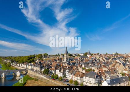 Vue aérienne panoramique de la Charite sur Loire dans le centre de la France, mettant en évidence le pont de pierre historique, les toits denses, la flèche de l'église et les formations nuageuses frappantes dans un ciel bleu vif. L'image capture le mélange d'architecture médiévale et de paysage riverain pittoresque le long de la vallée de la Loire. Banque D'Images
