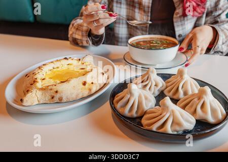 Femme ayant un repas géorgien authentique avec un bol de soupe Kharcho, pain au fromage khachapuri, et boulettes de viande khinkali Banque D'Images