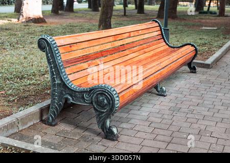 Banc de parc vide en bois doté de supports décoratifs en fonte, invitant à la détente et offrant un lieu de repos dans un cadre de parc urbain Banque D'Images