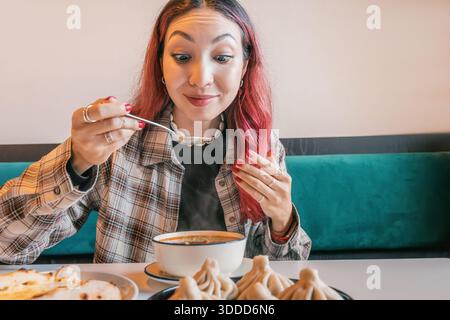 Femme dégustant une soupe chaude de kharcho dans un café avec une assiette de boulettes traditionnelles de khinkali géorgiennes, appréciant une cuisine régionale authentique Banque D'Images